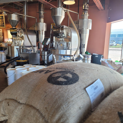 Close-up of a coffee roasting machine with a burlap bag in the foreground.