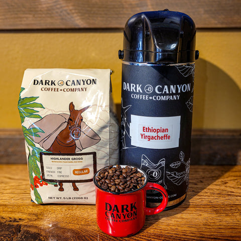 Dark Canyon Coffee Company packaging including a bag, mug, and airpot on a wooden counter.